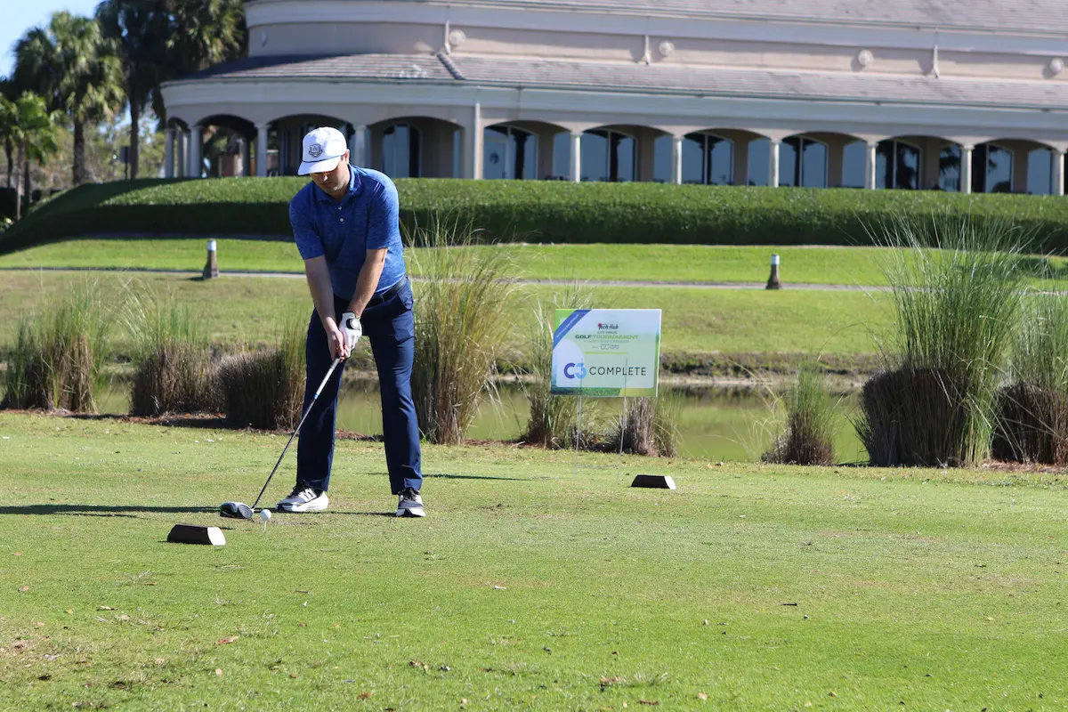 Golfer at the tee box during the Tech Hub Golf Invitational at Plantation Preserve featuring C3 Complete sponsorship signage.